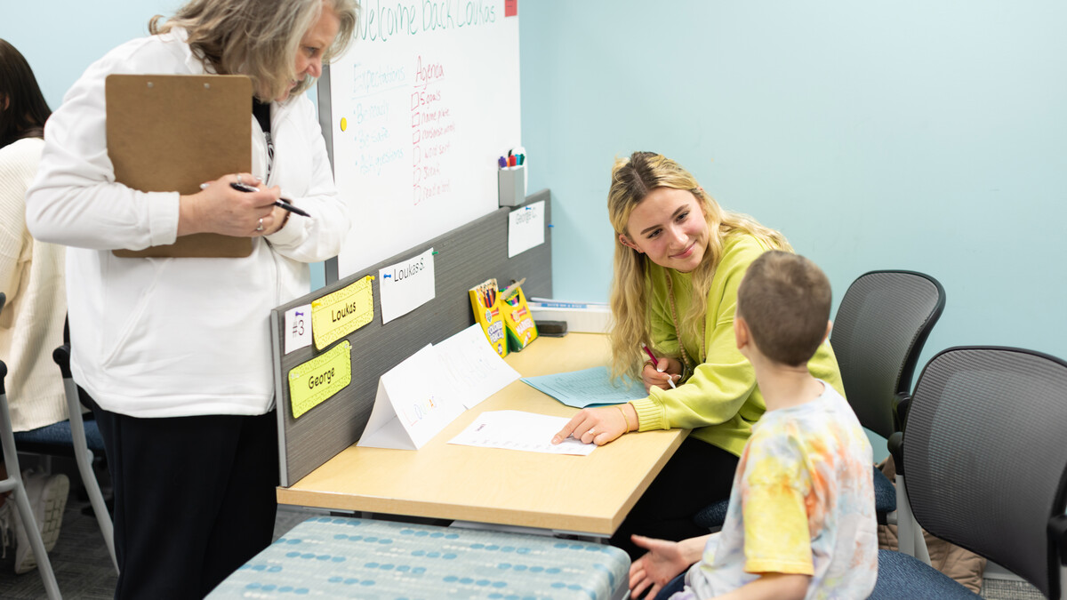Addie Olson (center), a senior elementary education major, works with a young male student at a desk in the Kit and Dick Schmoker Reading Center on Feb. 24 as Susan Dinsdale (left), a supervisor, observes.