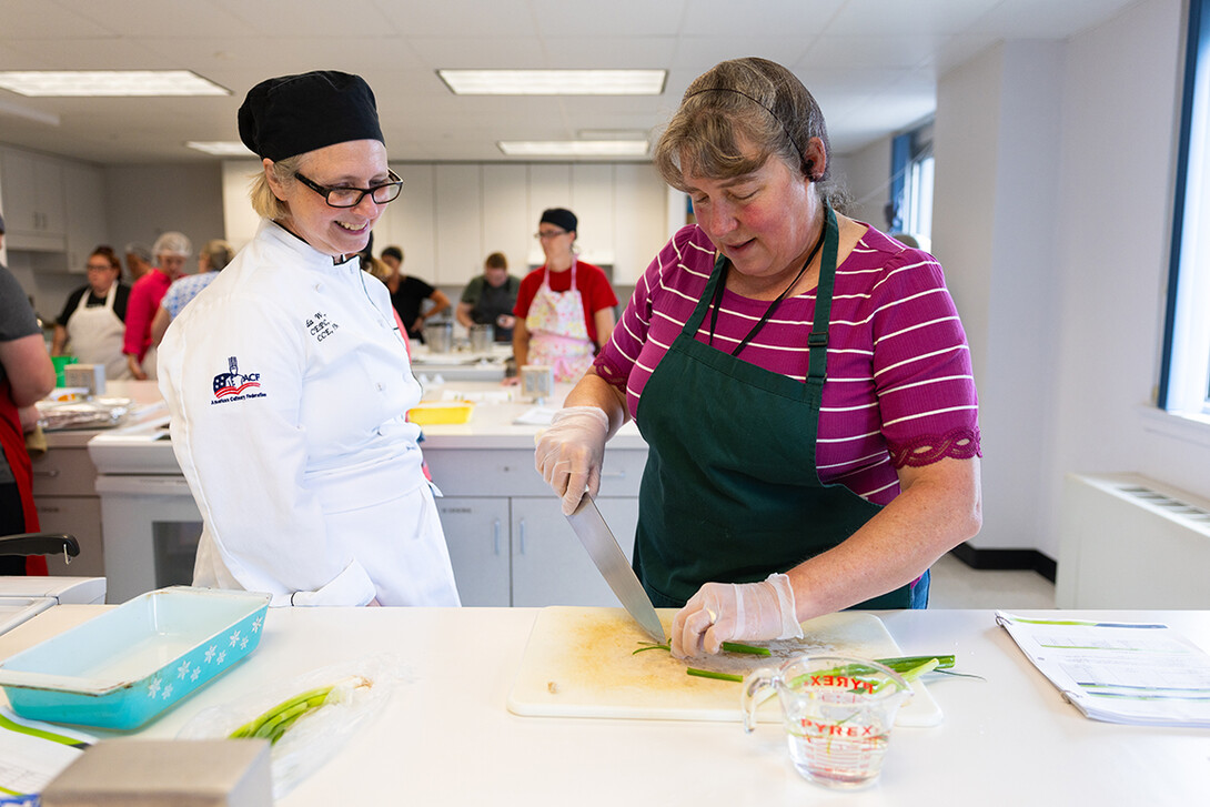Brenda Windmuller stops to chat with Renee Cornett, food and nutrition services operations manager for Gretna Public Schools, as she cuts thin strips into green onions.